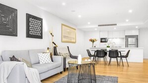 A modern living room with a grey sofa, a coffee table, and a dining area with chairs and a small table.
