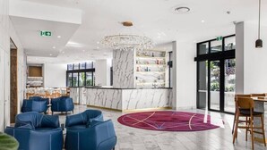 A modern lobby with marble flooring, blue seating, a central marble column, and a chandelier.