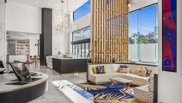 A modern interior with a reception desk, a seating area with a patterned rug, and large windows offering a view of the outdoors.
