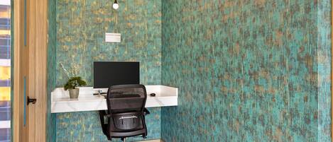 Un espacio de trabajo con un escritorio blanco, una silla de oficina negra, una planta en maceta y un letrero que indica un centro de negocios.