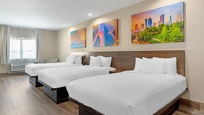 A hotel room with two beds, a large window with curtains, and three cityscape paintings on the wall. - Clarion Pointe Spring - Houston North (Spring)