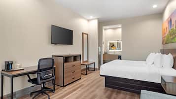 Una habitación de hotel con cama, escritorio, silla y televisor montado en la pared.