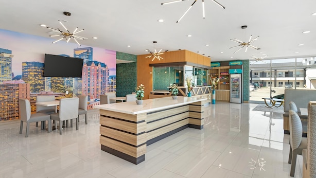 A modern hotel lobby with a central reception desk, seating area, and a cityscape mural on the wall. - Clarion Pointe Spring - Houston North (Spring)