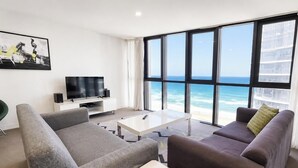 A modern living room with a large window overlooking the ocean, a flat-screen TV, and contemporary furniture.