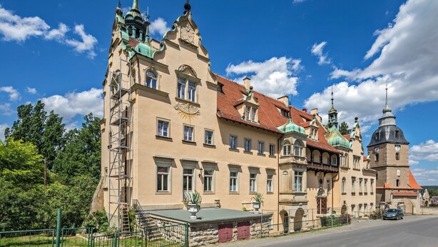 Ein historisches Gebäude mit verschiedenen Baustilen, darunter ein Turm mit einer Uhr, und einer gepflegten Fassade.