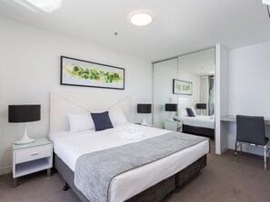 Une chambre d’hôtel moderne avec un grand lit, des tables de chevet avec des lampes, un bureau et un miroir.