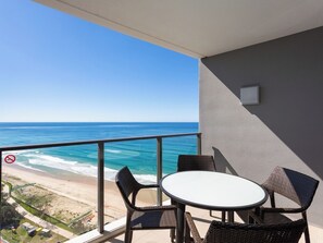 Un balcon avec vue sur l’océan et la plage, aménagé avec des fauteuils en osier et une table ronde.