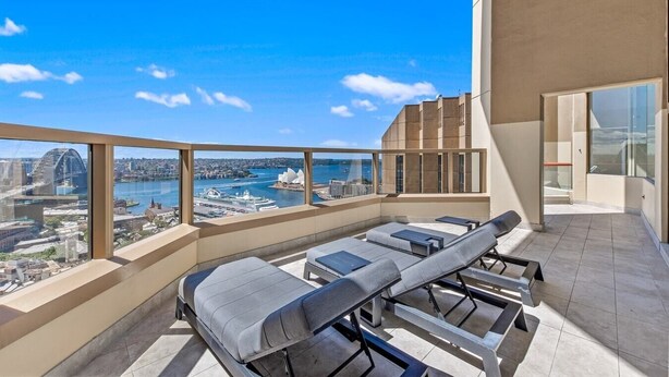 Un balcon doté de chaises longues, offrant une vue sur le paysage urbain, notamment un pont et un port.
