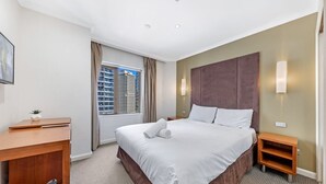 Une chambre d’hôtel avec un grand lit, un bureau, une chaise, une table de chevet et une fenêtre donnant sur la ville.