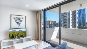 Ein modernes Wohnzimmer mit Fernseher, einer Couch und einem Balkon mit Blick auf die Stadt.