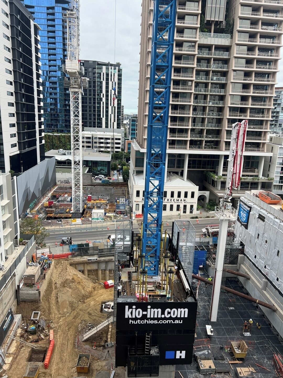 A construction site with a blue crane, buildings in the background, and a sign for 'kio-im.com'.