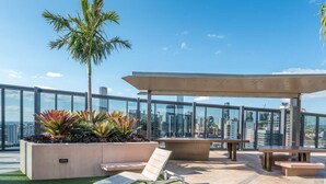 Una terraza en la azotea con una palmera, macetas con suculentas, una silla de descanso, una mesa y una pérgola.