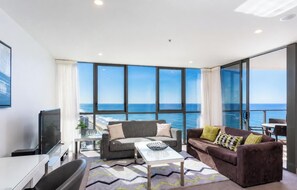 A modern living room with a large window overlooking the sea, a flat-screen TV, a sofa, and a coffee table.