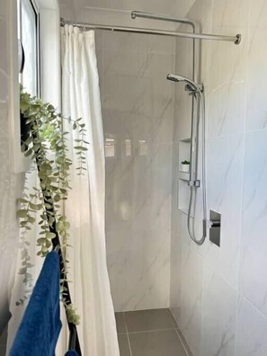 A modern shower area with a glass door, a towel rack with a blue towel, and a potted plant. - Convenient 2BR Unit in Salisbury | near TrainandBus (Salisbury)