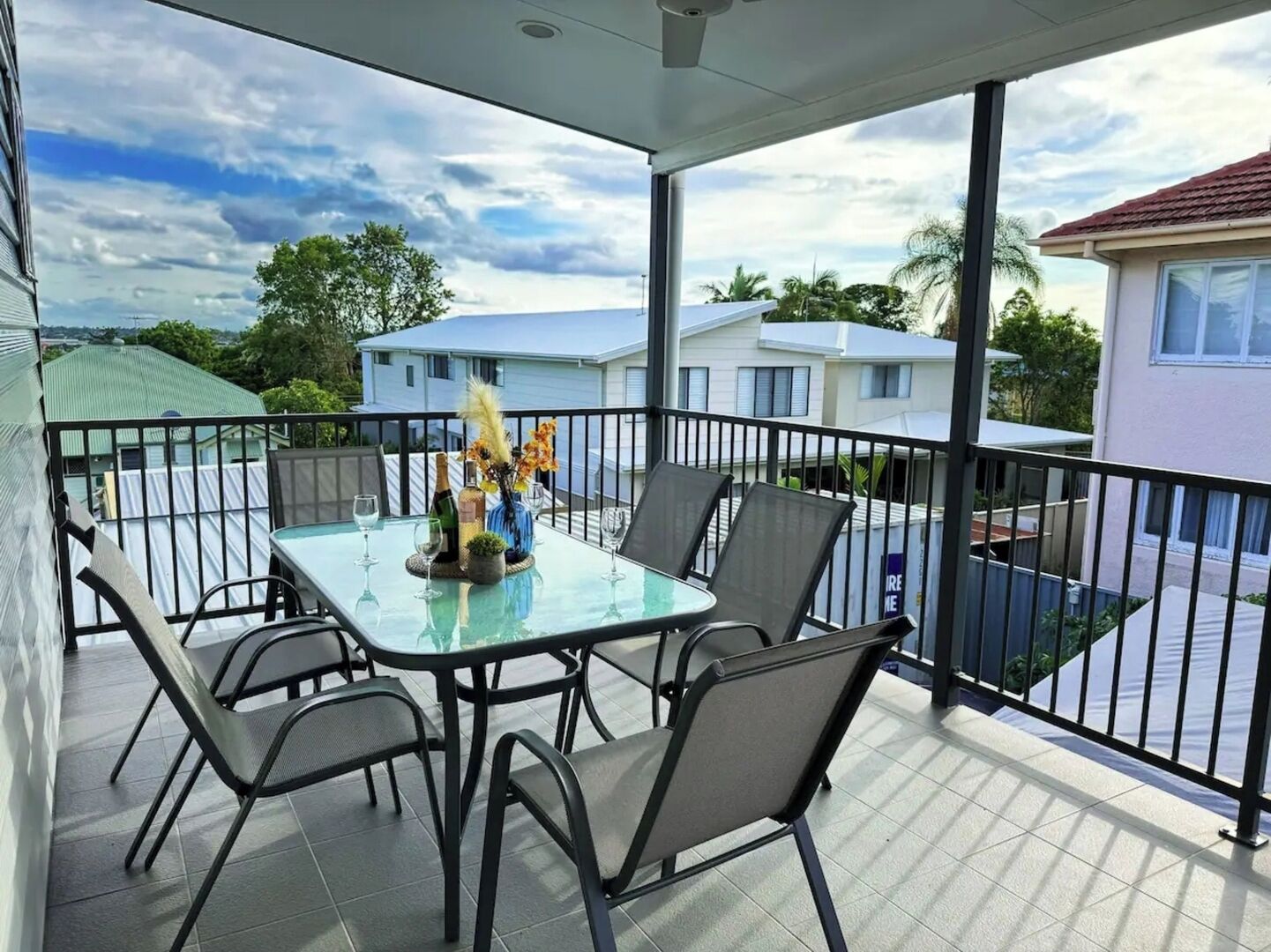 A balcony with a glass table and chairs, a bottle, and a vase with flowers.