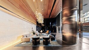 Un hall d’entrée moderne avec un plafond en bois, un espace de détente central agrémenté de canapés et de tables, et une grande colonne cylindrique.