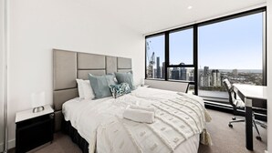 Une chambre d’hôtel moderne, dotée d’un grand lit, d’un bureau et offrant une vue sur le paysage urbain grâce à de grandes fenêtres.