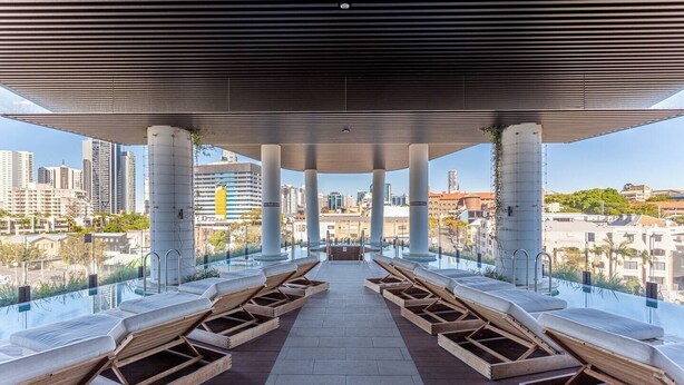 A rooftop infinity pool area with wooden loungers and a clear view of the city skyline. - Elegantandmodern 1 bedroom Apartment Infinity Pool (Fortitude Valley)
