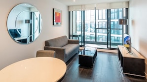 A modern living room with a sofa, a round table, and a coffee table. There is a large window with a city view, a round mirror, and a painting on the wall. - Elegantandmodern 1 bedroom Apartment Infinity Pool (Fortitude Valley)