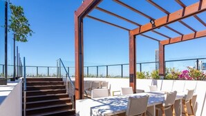 Una terraza en la azotea con una mesa, sillas, una escalera y vistas del horizonte urbano.