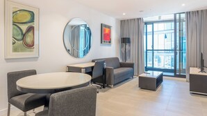 Una sala de estar moderna con una mesa de comedor redonda, sofá gris y un amplio ventanal con cortinas.