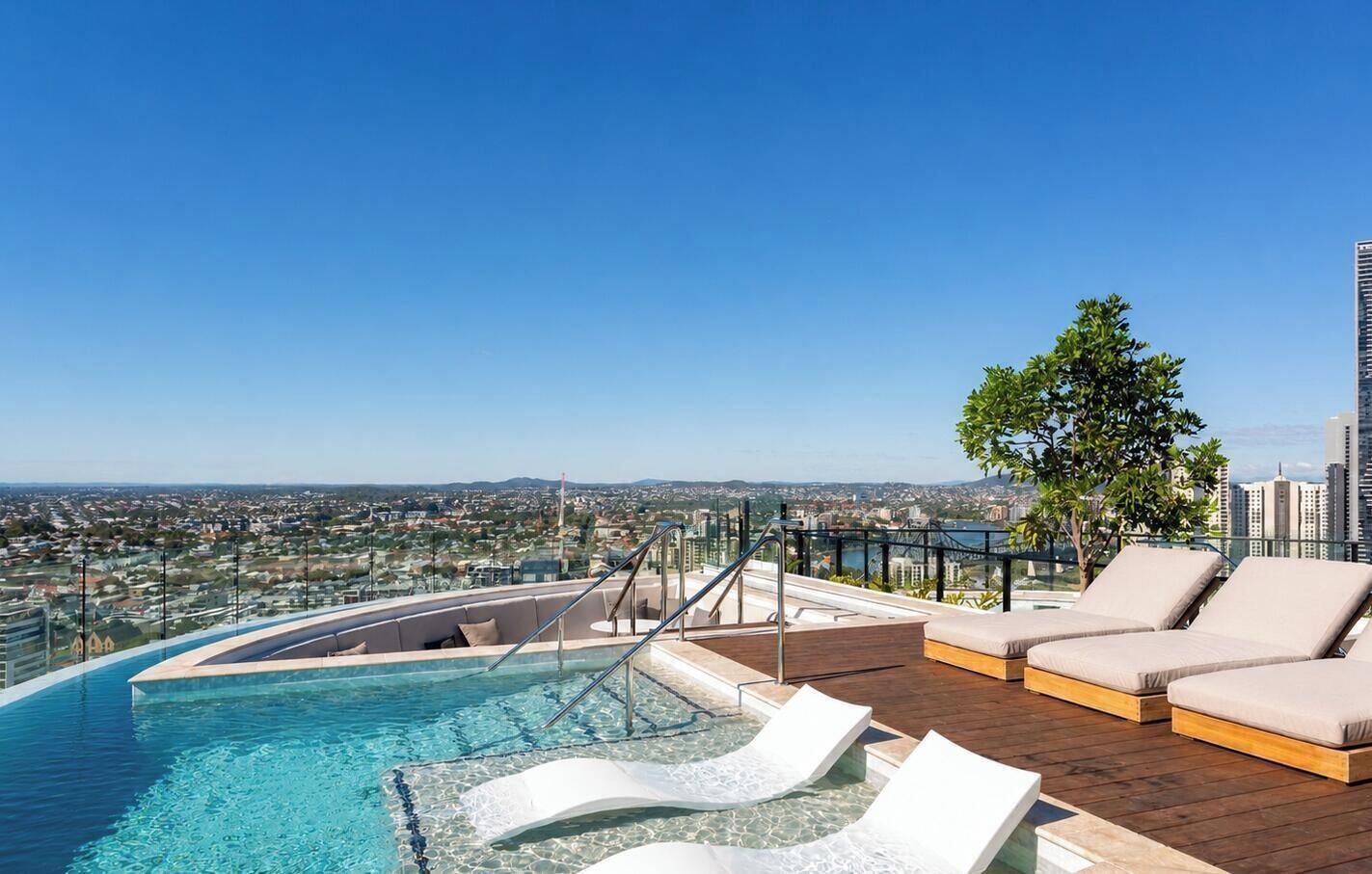 Una piscina infinita con vistas a la ciudad, sillas de descanso y una terraza de madera.
