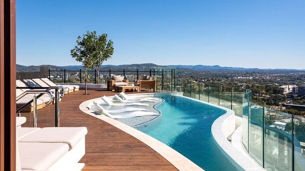 Piscina infinita en la azotea con sillones de descanso y barandilla de vidrio con vistas a la ciudad.
