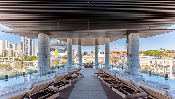 A rooftop infinity pool with wooden loungers, a clear view of the cityscape, and a modern architectural design.
