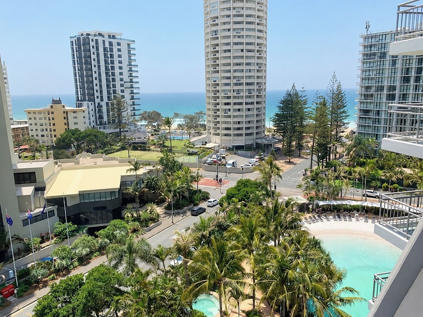 A high-rise hotel with a pool, palm trees, and a view of the ocean.