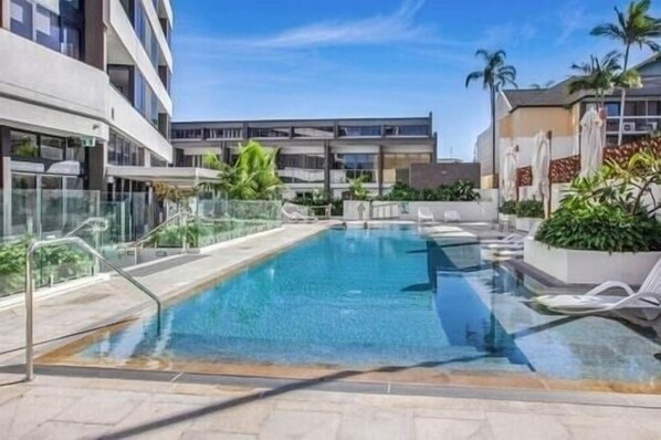 A swimming pool with clear blue water, surrounded by a glass barrier and white lounge chairs. - Open Ocean view 2 bedroom Apartment in Central (Surfers Paradise)