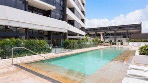 A modern building with a swimming pool, outdoor seating, and a clear sky. - Convenient Located 2-Bedroom Apartment In Surfers (Surfers Paradise)