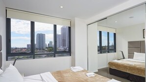 A modern hotel room with a large bed, a smaller bed, a desk, and a large window offering a city view. - Convenient Located 2-Bedroom Apartment In Surfers (Surfers Paradise)