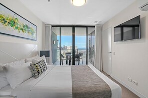 Quarto de hotel moderno com uma cama grande, uma televisão e uma varanda vista para a cidade.