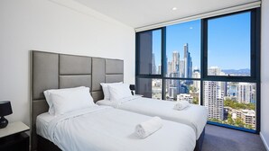 A hotel room with two beds, a large window with a city view, and a nightstand with a lamp.