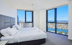 A modern hotel room with a large bed, a headboard, and a view of a cityscape and water. - Splendid Ocean and River view 3 Bedroom Apartment (Surfers Paradise)