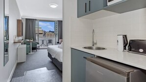 Ein modernes Hotelzimmer mit Küchenzeile, einem Bett, einer kleinen Essecke und Blick auf die Stadt.