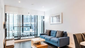 Un salon moderne avec un canapé, une table basse et une porte vitrée donnant sur un espace extérieur aménagé pour se détendre.