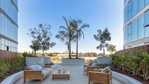 Une terrasse sur le toit, aménagée avec des meubles en bois, des palmiers et offrant une vue sur les bâtiments.