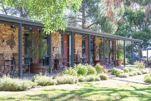 A covered outdoor seating area with brick walls and metal chairs, surrounded by a landscaped garden. - Comfy Studio 4 @ Blickinstal Barossa Valley (Bethany)