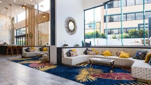 Un hall d’hôtel moderne doté d’un grand espace salon, d’un miroir décoratif et offrant une vue sur l’extérieur.