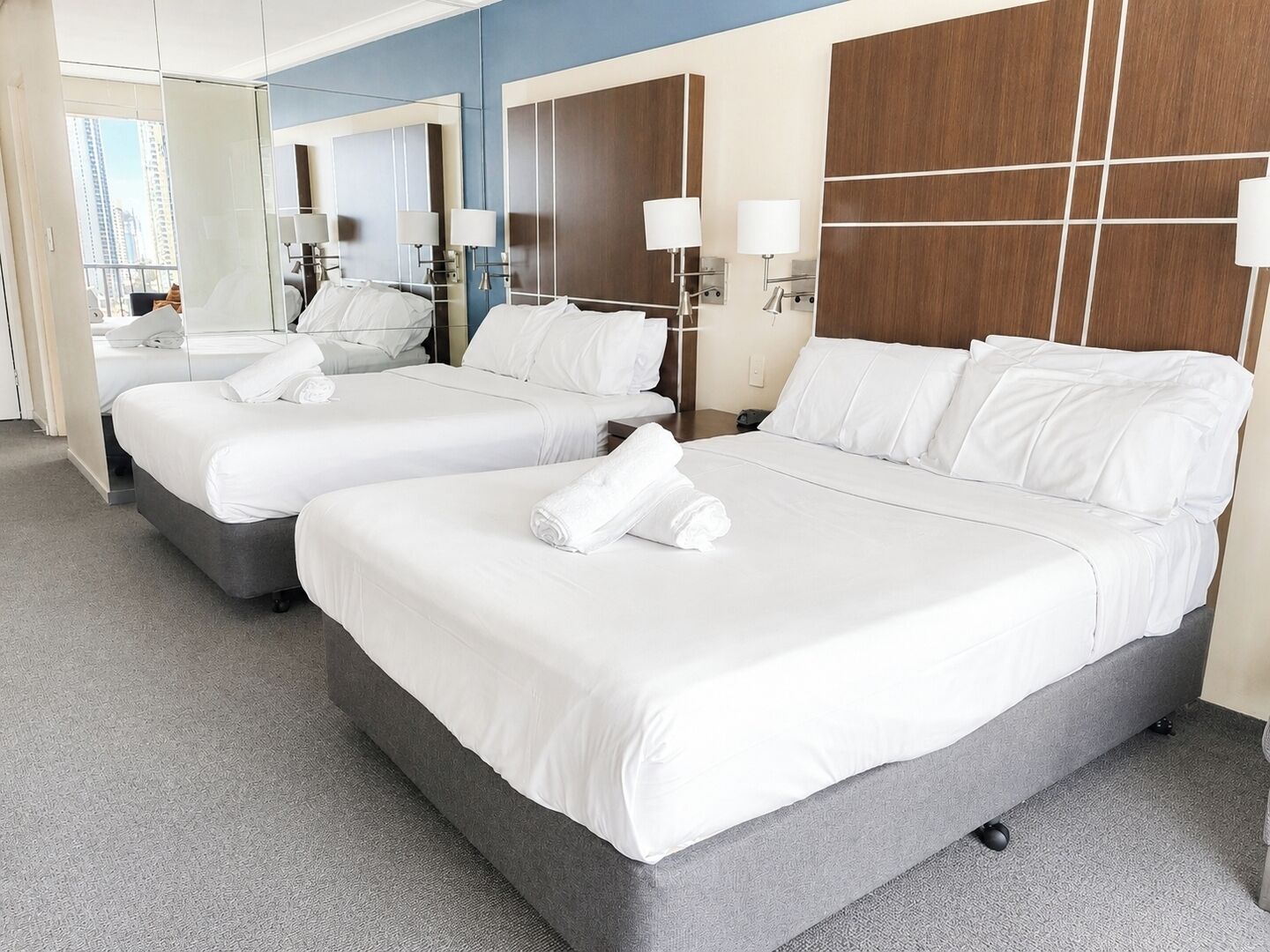 A hotel room with two beds, a large mirror, and a view of the city.