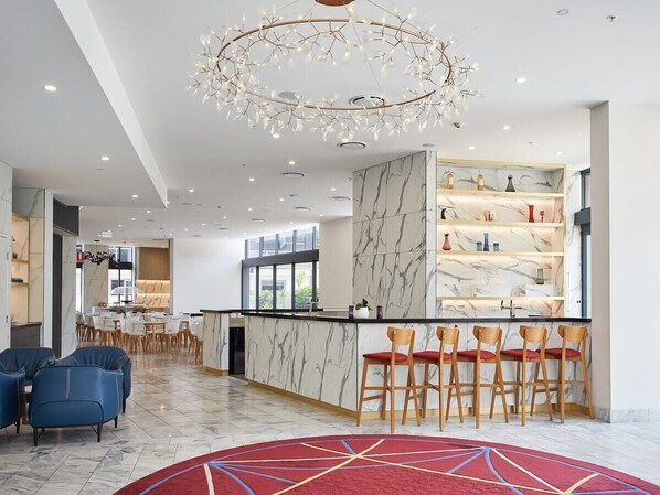 Un hall d’hôtel moderne avec un comptoir d’accueil en marbre, un bar et un lustre.