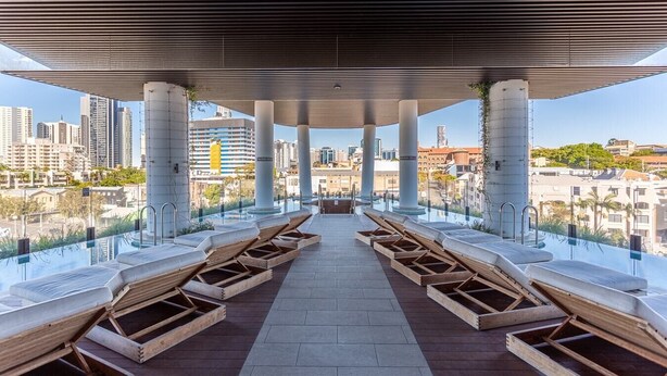 A rooftop infinity pool with wooden loungers and a view of the city skyline. - City View 1BR Apartment + ParkingandWalk to Station (Fortitude Valley)