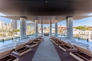 A rooftop infinity pool with wooden loungers and a view of the city skyline.