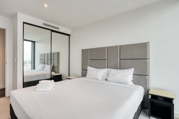 A modern hotel room with a large bed, a mirror, and a view of the city.