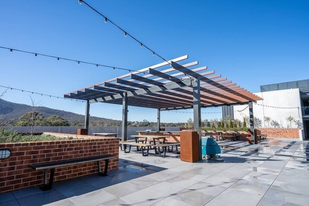 Un espace extérieur aménagé avec une pergola, des tables de pique-nique et un barbecue.