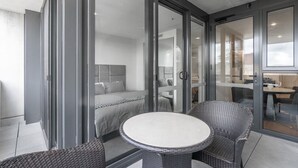 Una habitación de hotel moderna con un ventanal que da a un balcón con mobiliario de mimbre y una mesa redonda.