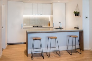 Una cocina moderna con una isla central, tres taburetes y una planta colgante.