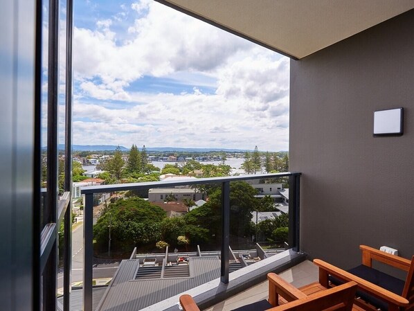 A balcony with a view of a cityscape, a small seating area, and a modern building facade. - Iconic Surfer's Sweet one bedroom Home in Surfers (Surfers Paradise)