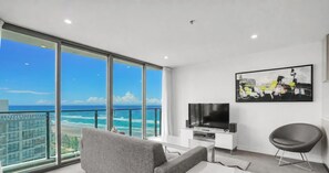 Ein modernes Wohnzimmer mit großem Fenster zum Strandblick, einem Flachbildfernseher und einem zeitgemäßen Sessel.